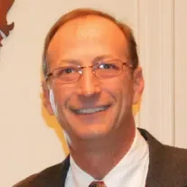 A man with glasses and a suit is smiling.